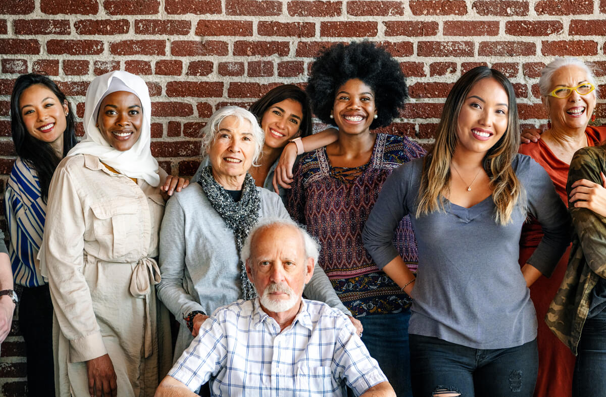 A group of diverse people together in front of a brick wall smiling at the camera. 